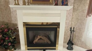A fireplace with a mantel, a vase of flowers, and a statue on the mantel. - Cozy 3-bedroom 2 bathroom house (Russell)