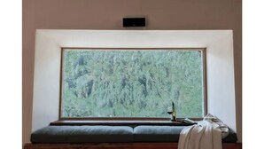 Ein Zimmer mit einem großen Fenster, einer Bank, einem kleinen Tisch mit einer Flasche und einer Fernbedienung an der Wand.