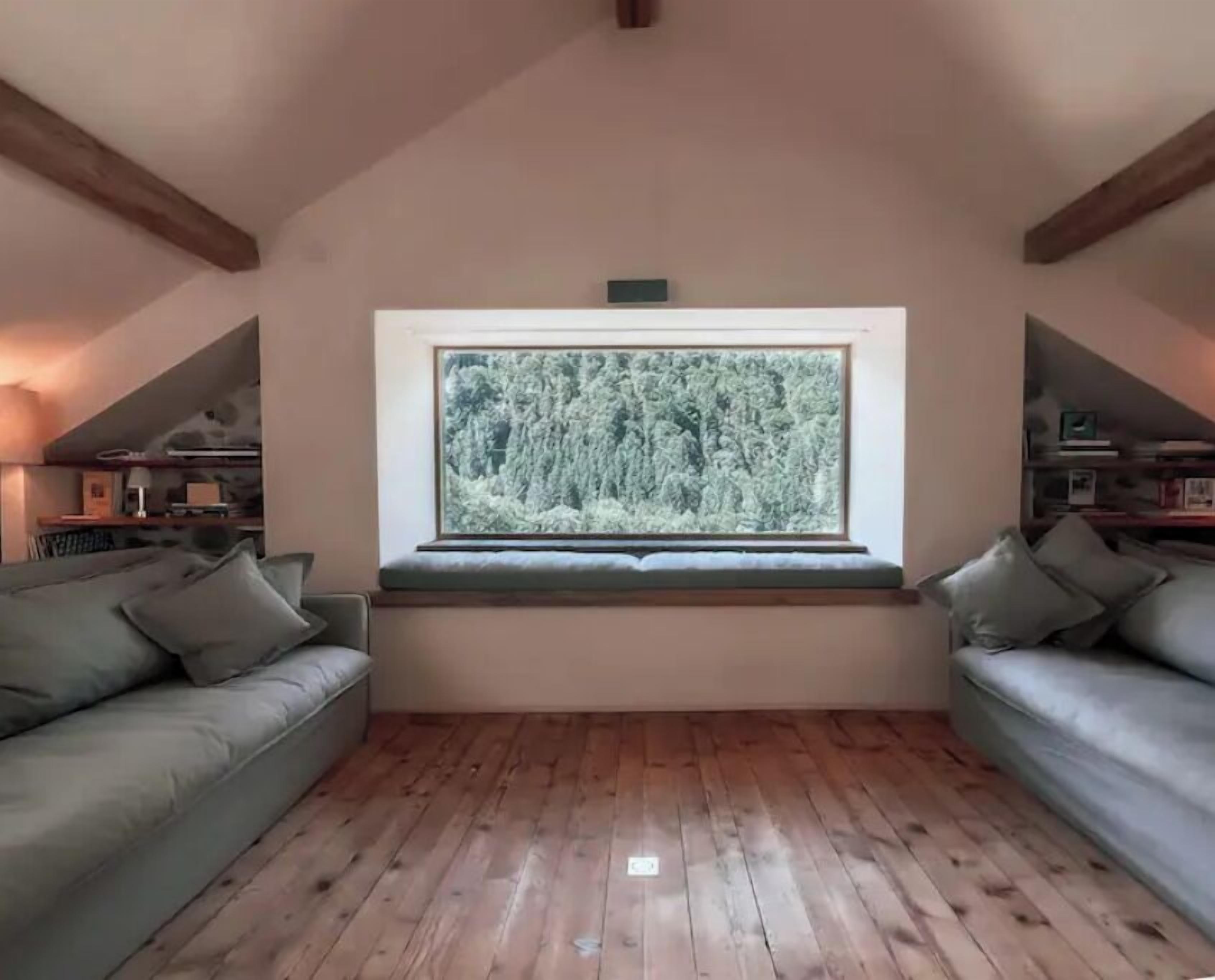 A room with a large window, wooden flooring, and two sofas.