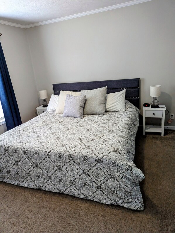A neatly made bed with a patterned bedspread, two bedside tables with lamps, and a dark headboard.