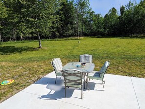 Un patio al aire libre con una mesa y sillas de vidrio, rodeado de césped y árboles.