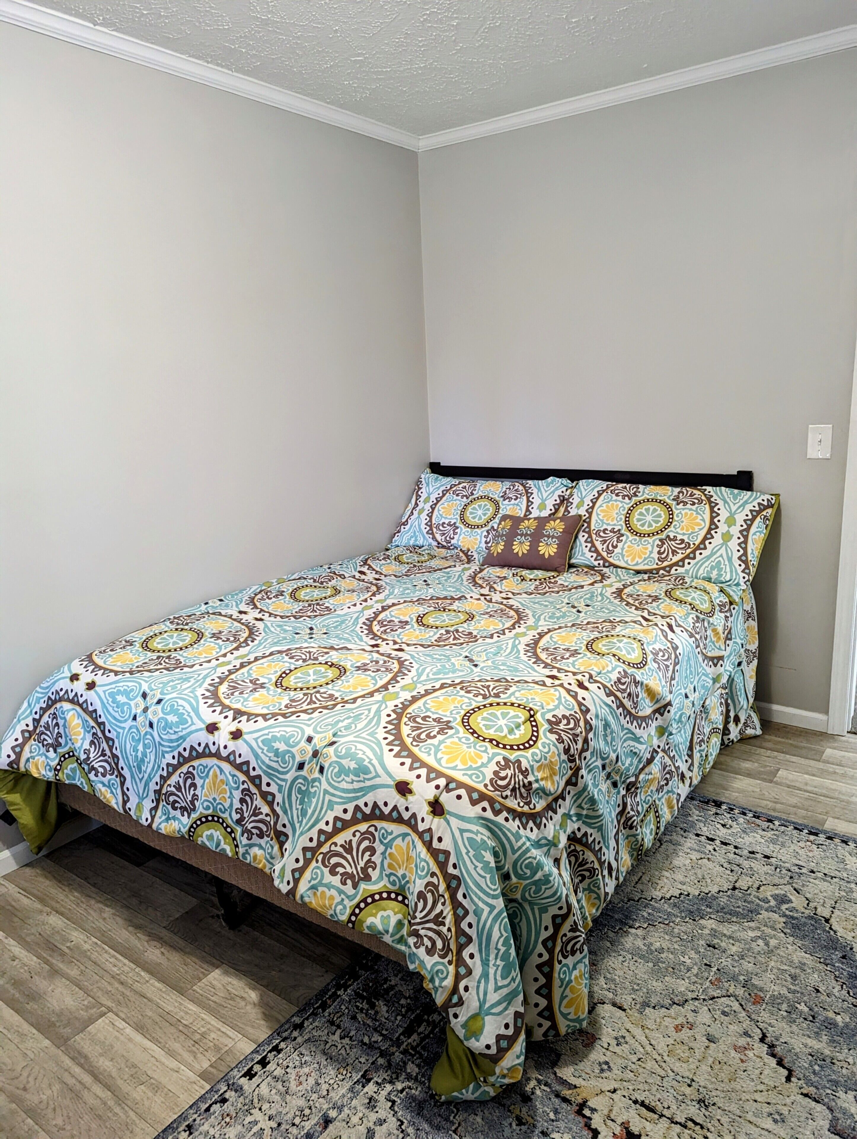 Una camera da letto con una coperta a motivi, una testiera e un tappeto sul pavimento.