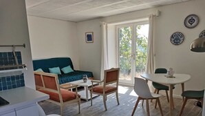 A compact living space with a sofa, dining table, chairs, and a kitchenette. - Centaurée** - Charm and countryside at a Witch on the Roof (Firmi)