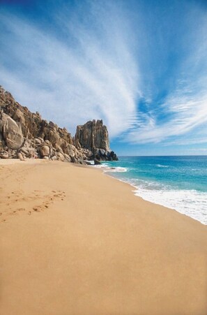 A beach with a rocky cliff and clear blue sky.