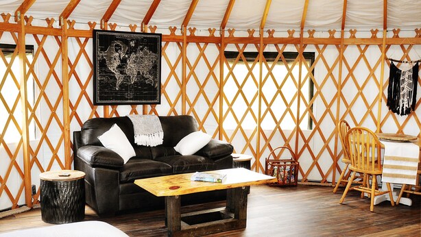 A cozy interior with a leather sofa, wooden coffee table, and a map on the wall. - Luxury Yurt for Couples with Hot Tub on Deck (Glenwood)