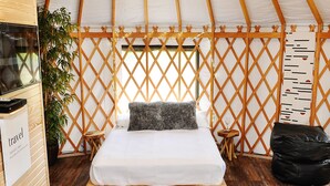 A cozy room with a bed, a small table, a chair, and a plant. - Luxury Yurt for Couples with Hot Tub on Deck (Glenwood)