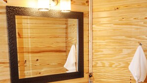 A wooden bathroom with a large mirror, a white sink, and shelves holding towels. - Luxury Yurt for Couples with Hot Tub on Deck (Glenwood)