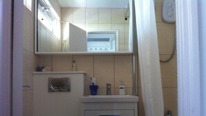 Un baño pequeño con inodoro, lavamanos con espejo y zona de ducha.