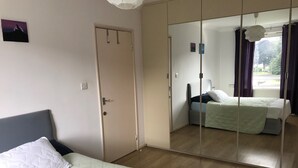 Un dormitorio con cama, armario, espejo y ventana con cortinas.