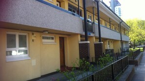 Un edificio de apartamentos de dos pisos con fachada plana, múltiples ventanas y un pequeño jardín frontal.