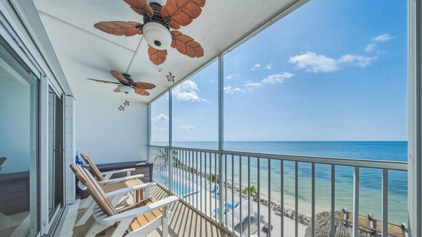 A balcony with a ceiling fan, a view of the ocean, and a seating area with chairs and a table. - Seaside Villa~ Charming Beachfront Condo w/ Pool! (Marathon)
