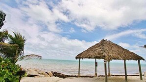 A beach with a thatched-roof hut, clear sky, and calm sea. - Seaside Villa~ Charming Beachfront Condo w/ Pool! (Marathon)