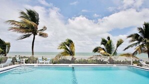 A pool with a white fence, palm trees, and a view of the ocean. - Seaside Villa~ Charming Beachfront Condo w/ Pool! (Marathon)