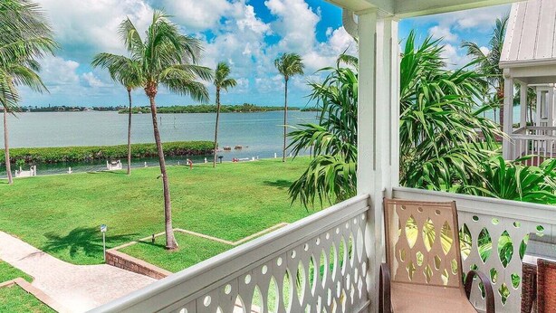 A balcony with a view of a grassy area and palm trees, overlooking a body of water. - Indigo Reef #50 ~ The Palms, Sunset Views & 31' Boat Slip (Marathon)