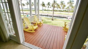 A wooden deck with yellow chairs and a view of palm trees and a body of water.
