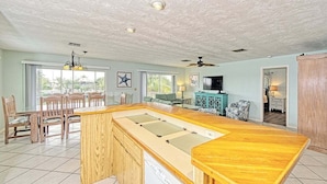 A spacious kitchen with a wooden island, a dining area with chairs, and a television in the living room. - One Particular Harbor ~ Waterfront Pool Home Near the Beach! (Marathon)