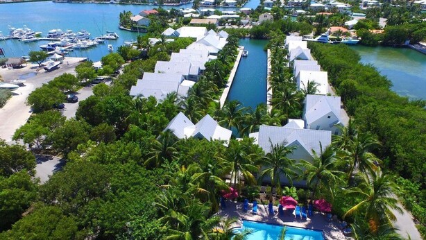 Ein Resort mit einem zentralen Pool, umgeben von Palmen, und einer Marina mit Booten.