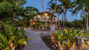 A pathway leading to a building surrounded by palm trees and tropical plants. - Sunsets in Paradise~ Gulf Front Pool Home, 22' Dock, Kayaks, Bikes & Paddleboards (Marathon)