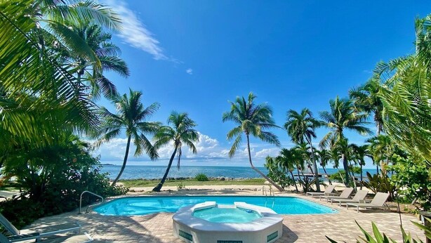 A pool area with lounge chairs and a hot tub, surrounded by palm trees and a view of the ocean. - Sunsets in Paradise~ Gulf Front Pool Home, 22' Dock, Kayaks, Bikes & Paddleboards (Marathon)