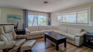 A living room with a beige sectional sofa, a wooden coffee table, and a dark wooden side table. - Sunsets in Paradise~ Gulf Front Pool Home, 22' Dock, Kayaks, Bikes & Paddleboards (Marathon)