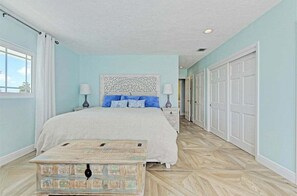 A bedroom with a large bed, two bedside tables, a decorative headboard, and a chest of drawers.