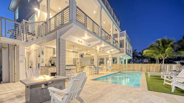 A modern house with a pool, outdoor seating, and a well-lit interior. - Casa Playa~ Luxury Pool Home Amazing Outdoor Area! (Marathon)