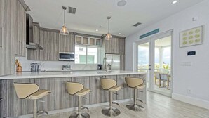 A modern kitchen with a central island, bar stools, and a view to the outside. - Casa Playa~ Luxury Pool Home Amazing Outdoor Area! (Marathon)