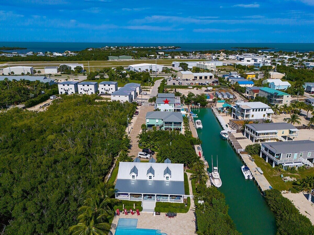 An aerial view of a coastal town with a marina, several buildings, and a large green area.