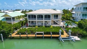 Une propriété située au bord de l’eau, avec une grande maison dotée de nombreux balcons, d’un quai et d’une végétation luxuriante.