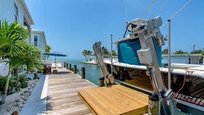 A wooden dock leading to a boat with a blue cover, palm trees, and a clear blue sky. - Island Time~ Pool Home Seconds to Open Ocean! 26' Dock (Marathon)