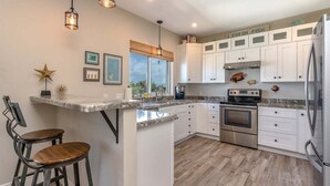 A modern kitchen with white cabinets, stainless steel appliances, and a bar area with two stools. - Island Time~ Pool Home Seconds to Open Ocean! 26' Dock (Marathon)