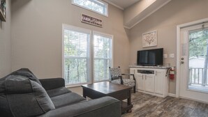 A living room with a gray sofa, a coffee table, a TV on a stand, and a sign that reads "Cabin Sweet Cabin".