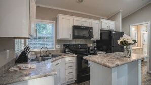 A modern kitchen with white cabinets, a black microwave, a black refrigerator, a stove, and a sink.
