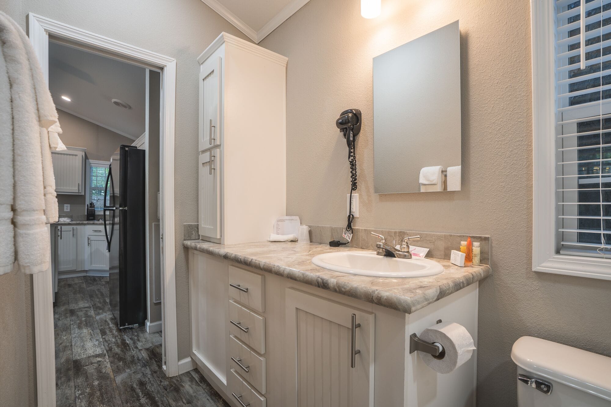 A bathroom with a sink, toilet, and a mirror. There is a towel rack and a hairdryer on the wall.