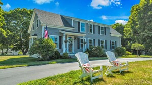 A two-story house with a porch, a flag, and two Adirondack chairs.