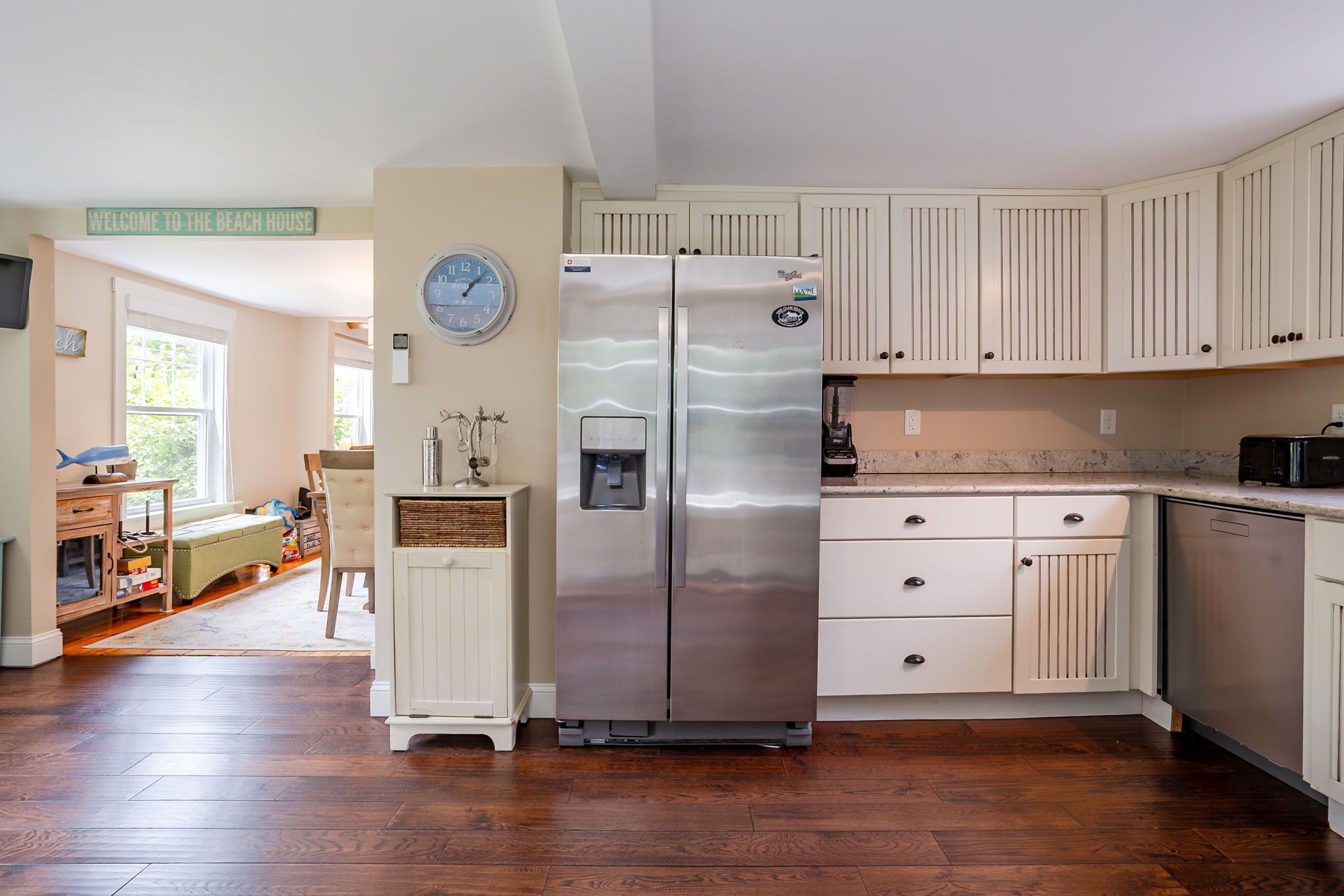 A kitchen with white cabinets, a stainless steel refrigerator, and a clock on the wall.
