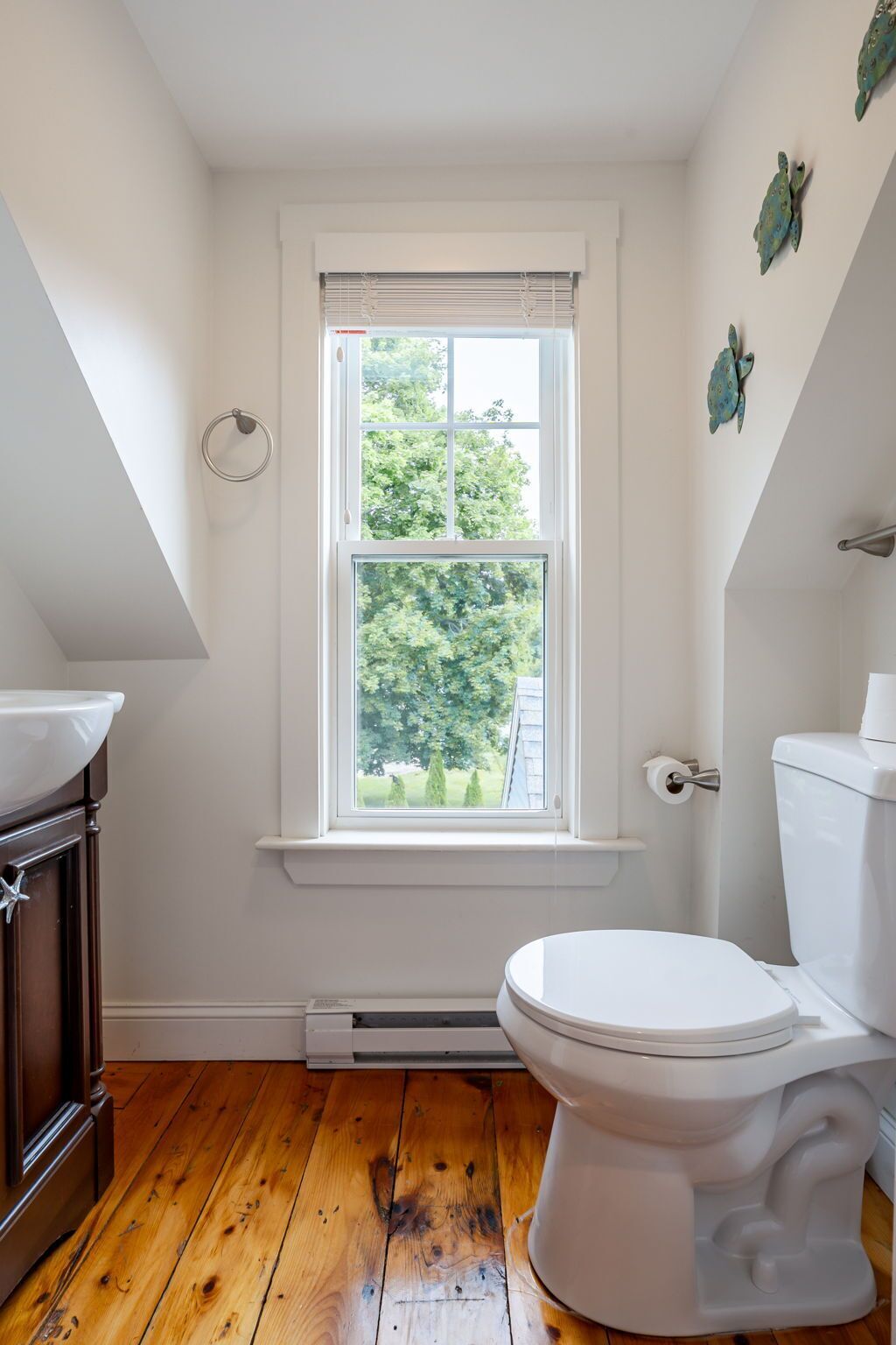 Un baño con inodoro blanco, una ventana con persianas, suelo de madera y un perchero para toallas.