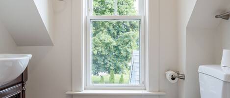 Un baño con inodoro blanco, una ventana con persianas, suelo de madera y un perchero para toallas.