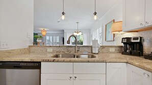 Una cocina con un lavamanos doble, armarios blancos, lavavajillas, luces colgantes y una cafetera.