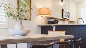 Un comedor con una mesa de madera, cuatro sillas negras, un florero con plantas y una lámpara colgante.