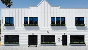 Un edificio blanco con tres puertas de garaje y numerosas ventanas, cada una con una jardinera.