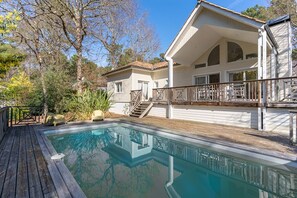 Ein zweistöckiges Haus mit Swimmingpool, Holzterrasse und überdachter Veranda.