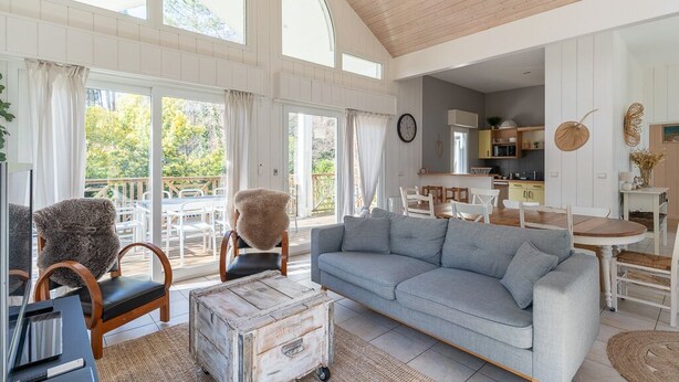 Ein großzügiger Wohnbereich mit grauem Sofa, Holzstühlen, einem Esstisch und einer Küche im Hintergrund.