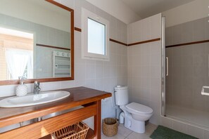 Ein Badezimmer mit einem Holzbadschrank, einem weißen Waschbecken, einer Toilette und einer Duschkabine aus Glas.
