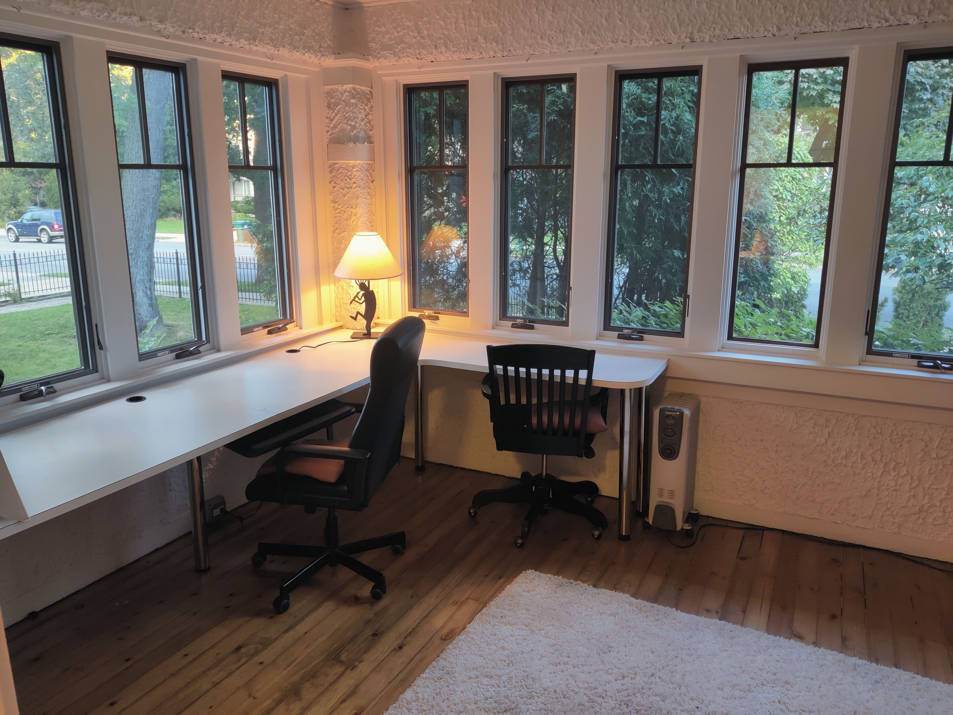 A home office with a desk, two chairs, a lamp, and large windows with a view of greenery.