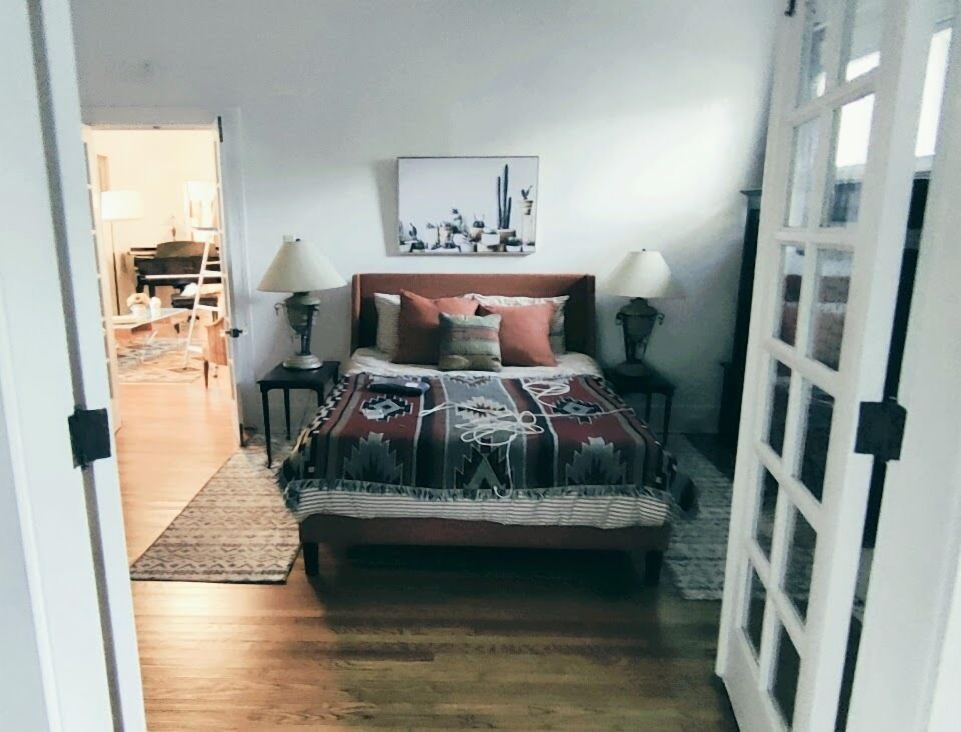 A bedroom with a bed, two bedside tables, a nightstand, a rug, and a wall-mounted picture.