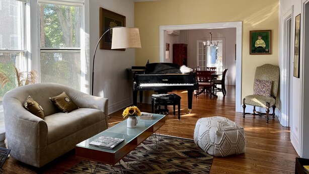 A spacious living room with a grand piano, a comfortable sofa, and a dining area with a chandelier. - Historic Oak Park Home (Oak Park)