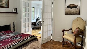 A room with a bed, a chair, a fireplace, a door leading to another room, and a painting on the wall. - Historic Oak Park Home (Oak Park)
