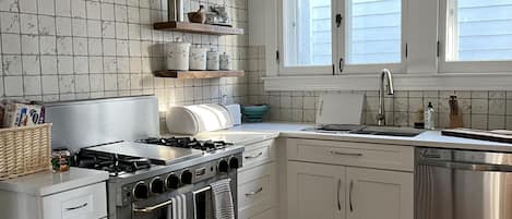 Een moderne keuken met witte kasten, een roestvrijstalen fornuis en een groot raam.