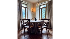 A dining area with a round table and four chairs, large windows with curtains, and a hanging light fixture. - Luxury hideaway in PDS - The Stonehouse Front Door (Saint-Jean-d'Aulps)